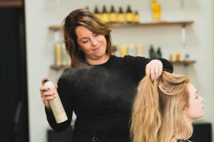 “Haarstylist in actie bij Atelier Puur-Haar, bezig met föhnen en stylen van lang blond haar in een natuurlijke eco-luxe kapsalon.”